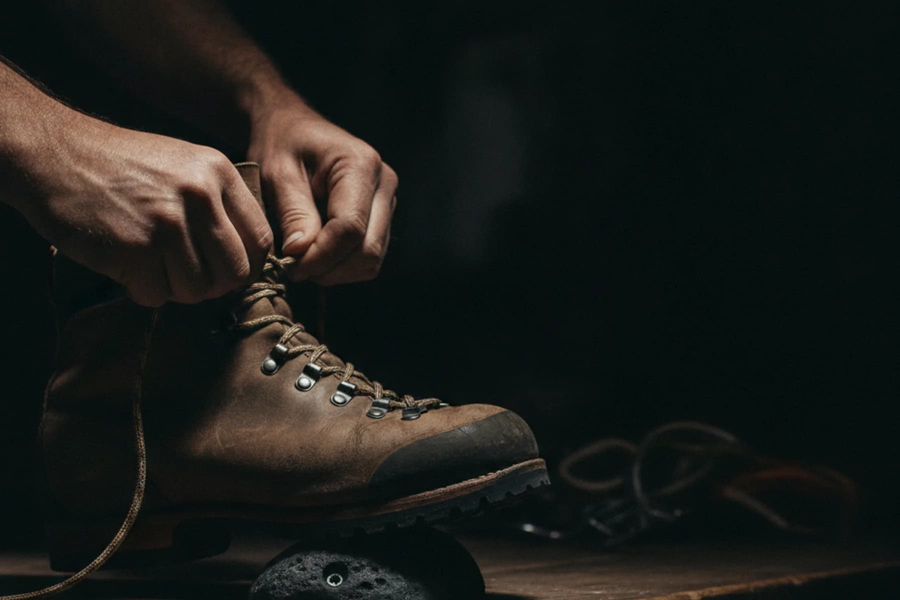 Hände schnüren einen Bergschuh an der Anprobe-Wand.